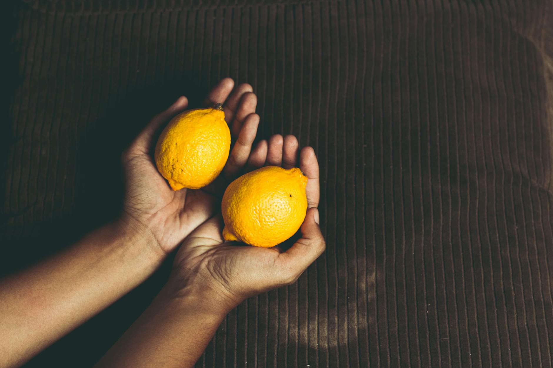 Primer plano de dos limones frescos en manos ahuecadas sobre superficie marrón, simbolizando frescura y cuidado