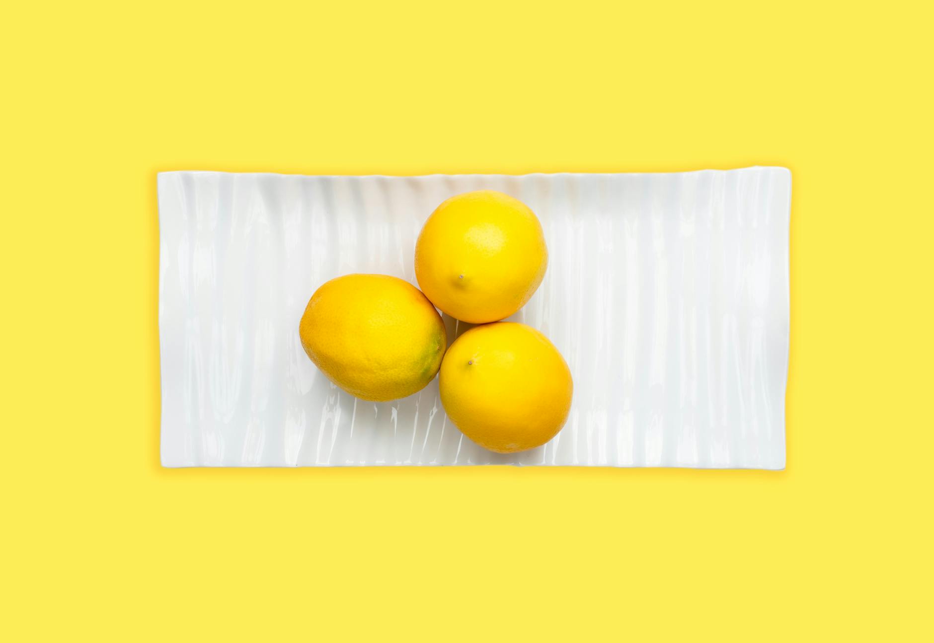 Hand holding a fresh lemon against a vibrant yellow background, representing fresh approaches to pleasure and sensation.