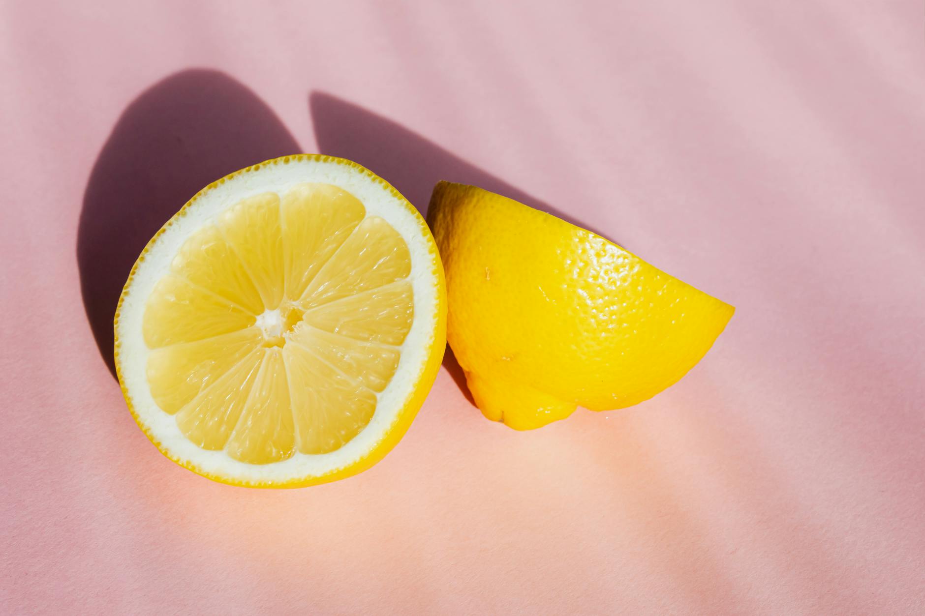 Fresh lemons arranged on a pink surface in natural sunlight, representing the Lem vibrator's bright citrus-inspired design