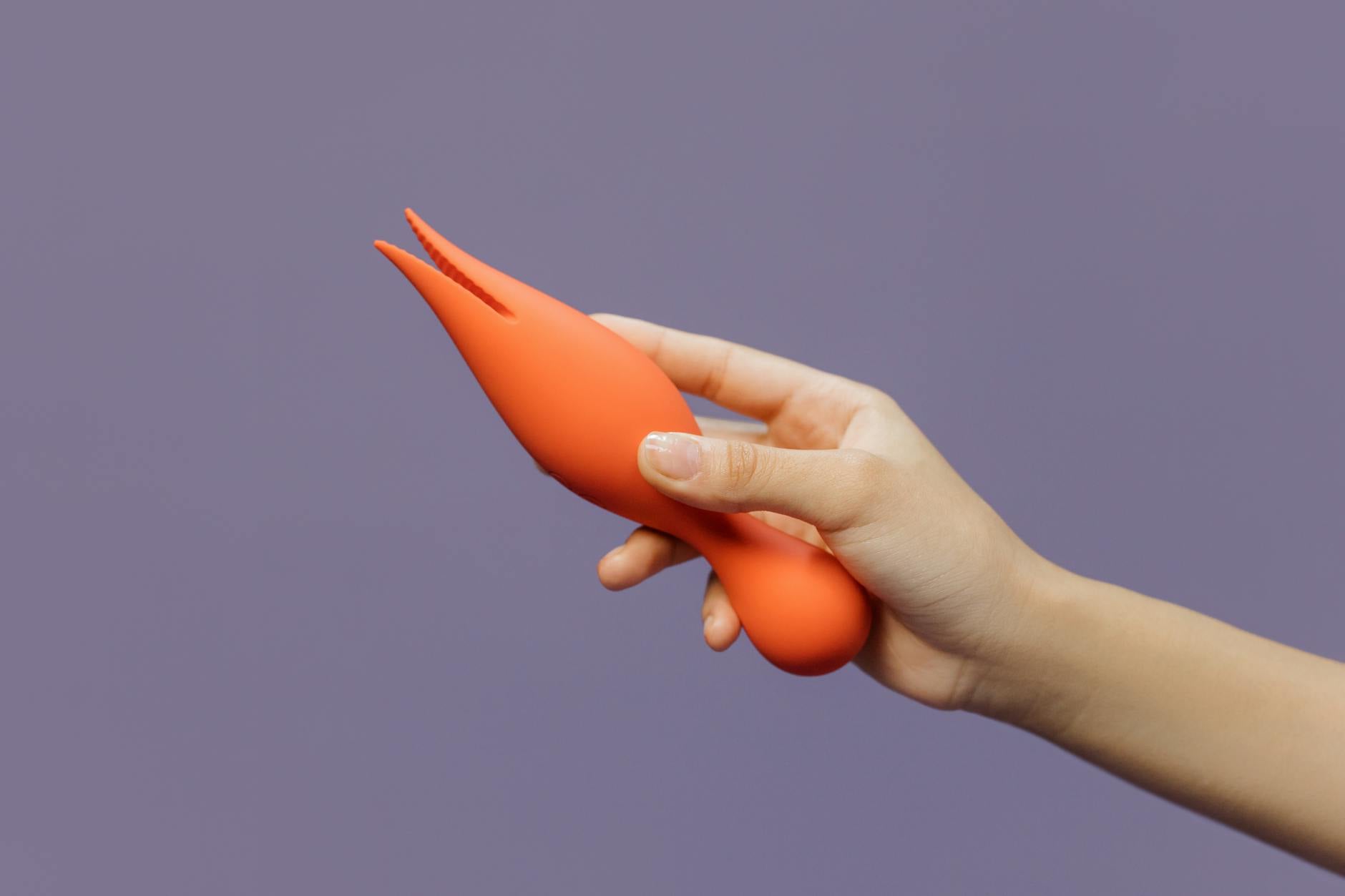 A vibrant orange clitoral vibrator held against a purple backdrop, representing modern sensuality and pleasure.