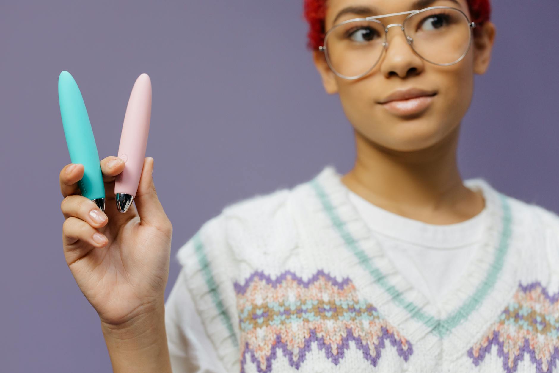 Person holding colorful vibrators against a purple background, representing body-positive pleasure