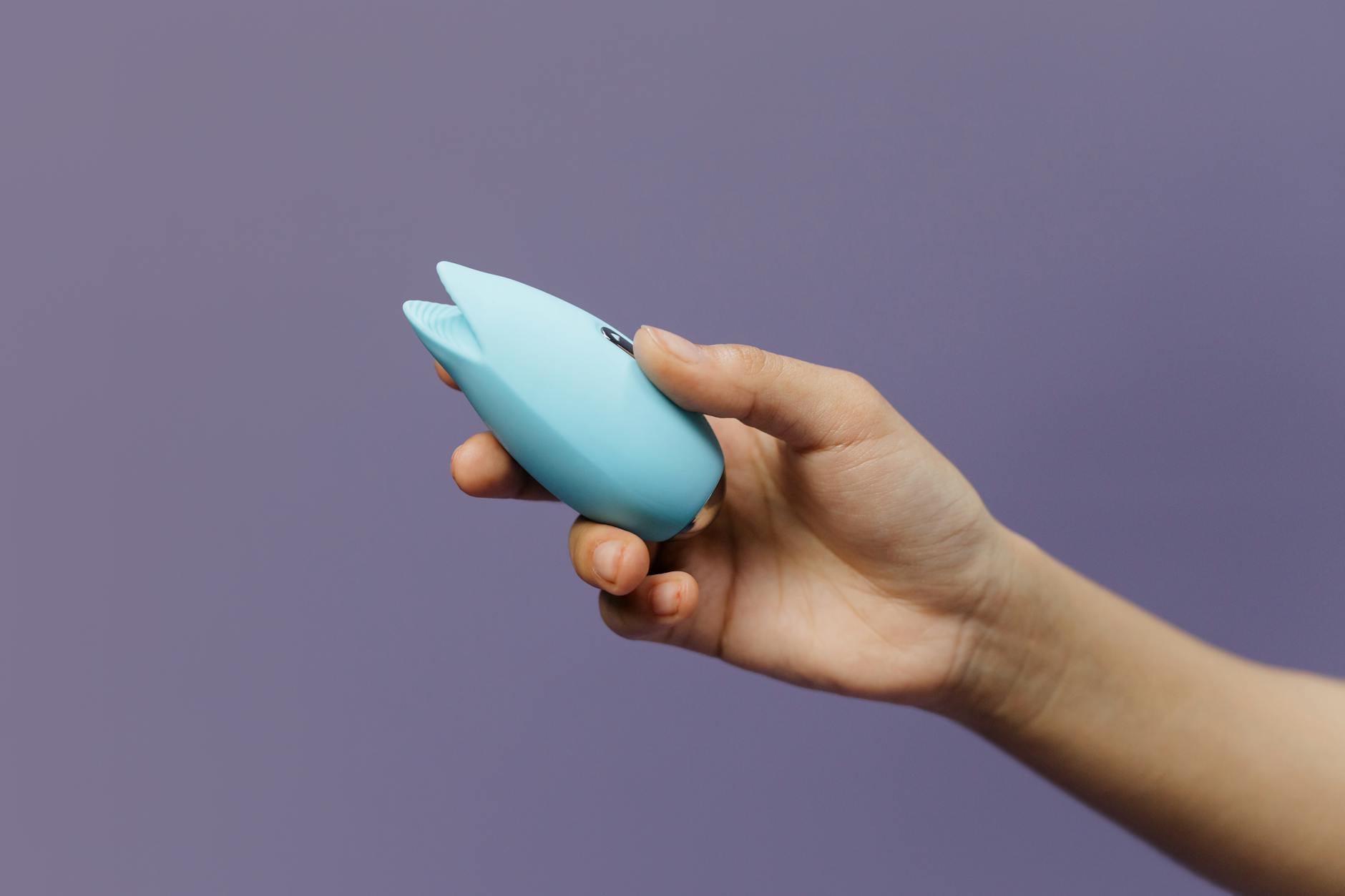 Mano sosteniendo vibrador de succión naranja contra fondo morado minimalista que promueve el amor propio y la sexualidad